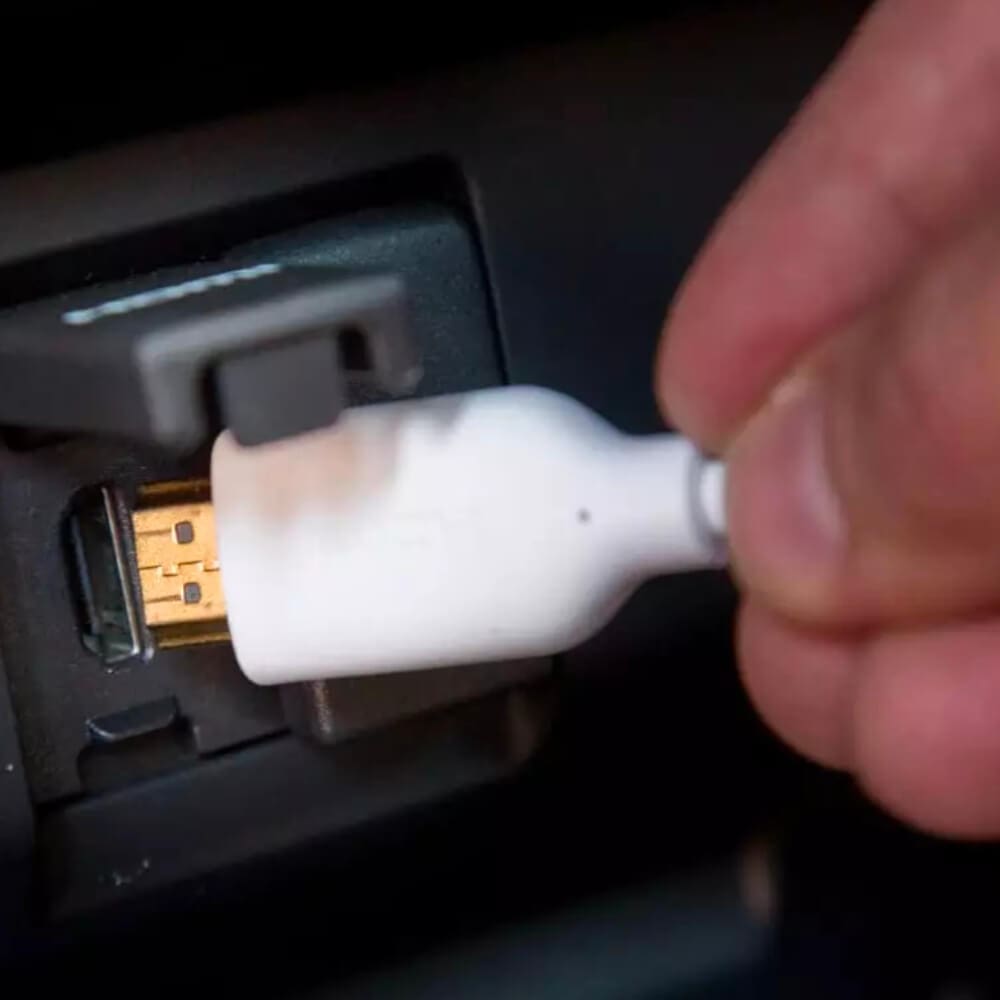 A hand is plugging a white adapter with visible burnt marks into a USB port, reminiscent of worn-out radio replacement parts. The dark background accentuates the connection area.